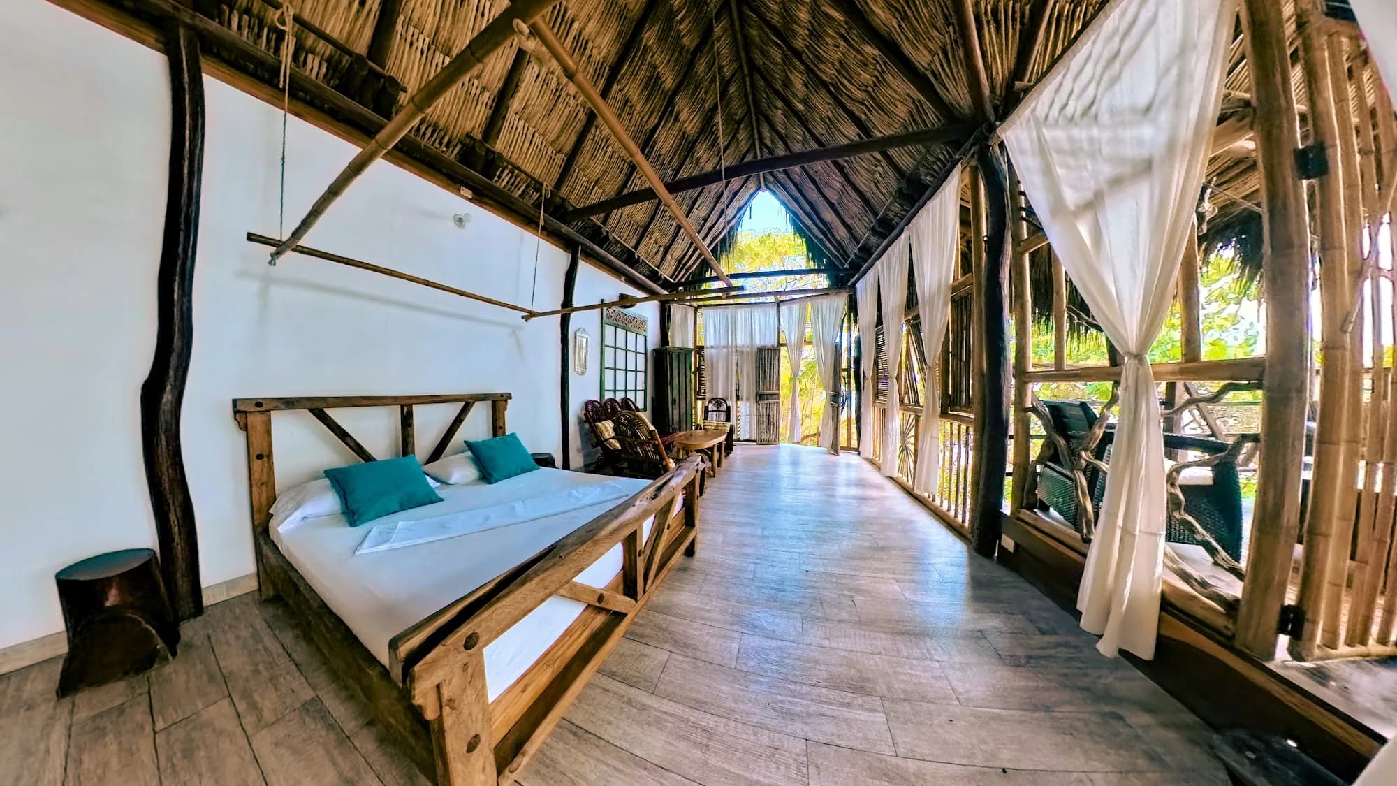 Interior de Casa del Mar: cama de madera bajo el techo de palma, abierta al corredor y a la vegetación