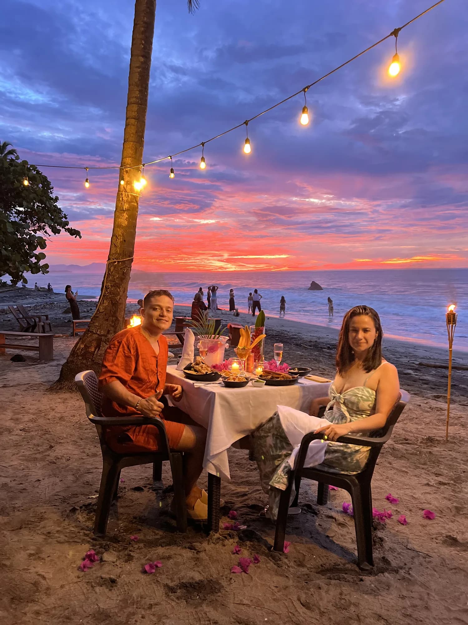 Mesa para dos en la playa al atardecer, con luces colgantes