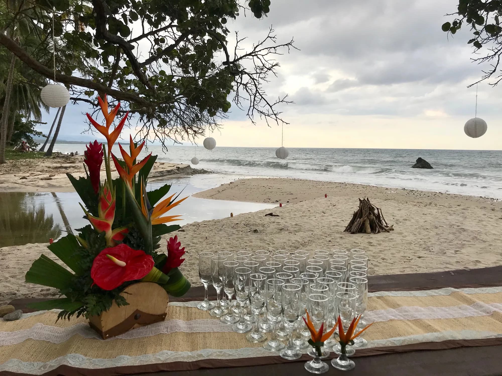 Montaje de evento en la playa al atardecer, con flores y copas