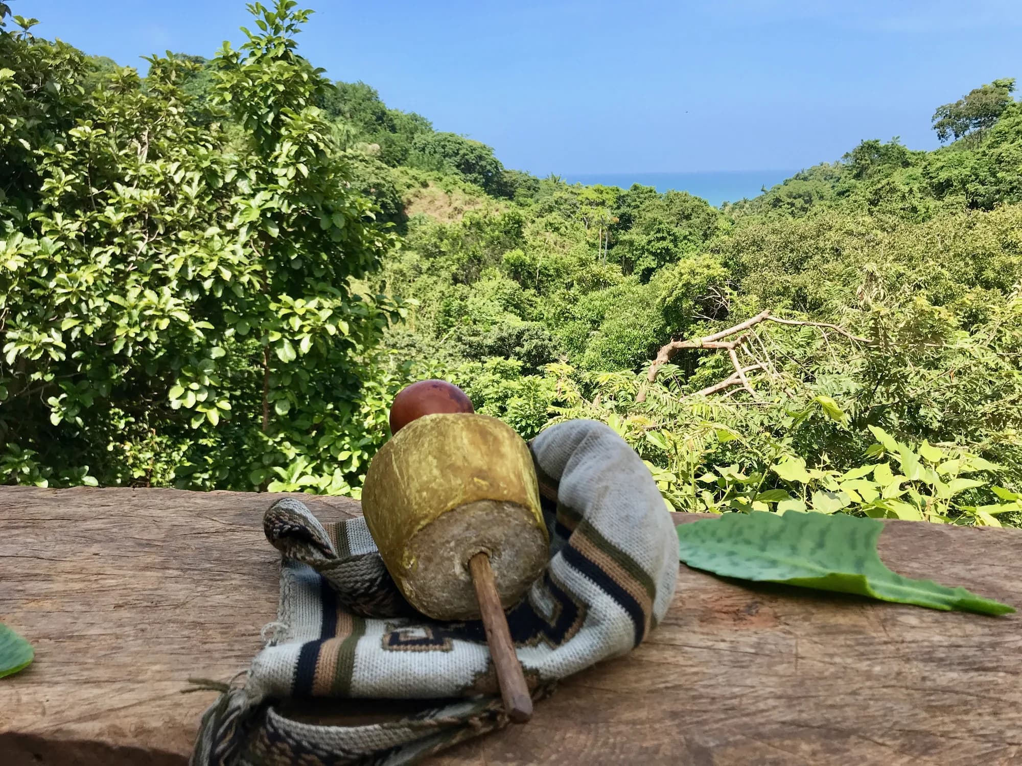 Poporo y mochila arhuaca sobre una mesa de madera, con el mar al fondo
